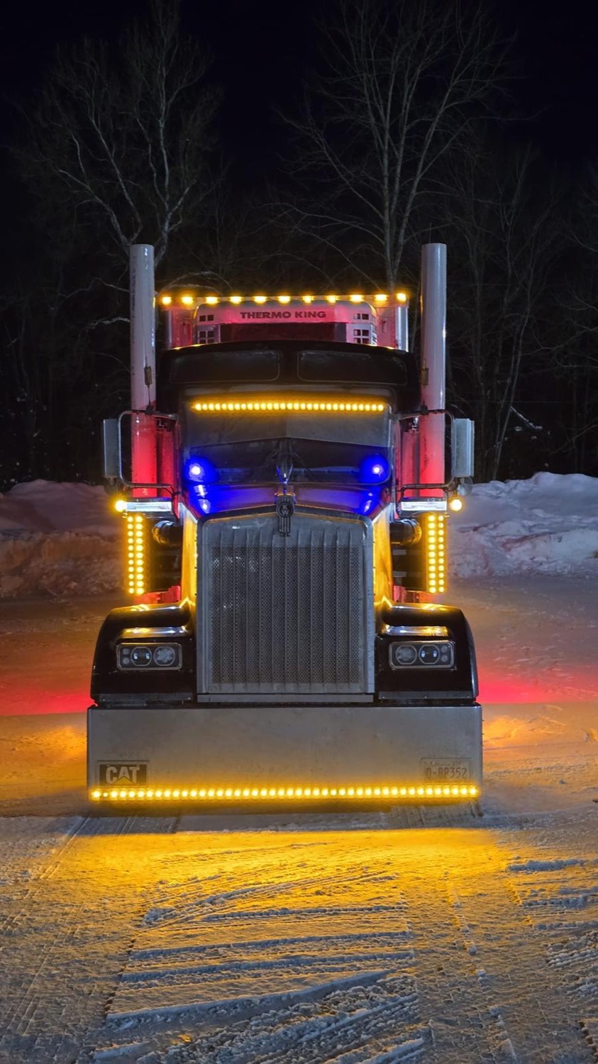 Black Kenworth on snow at night with amber and blue LED lighting
