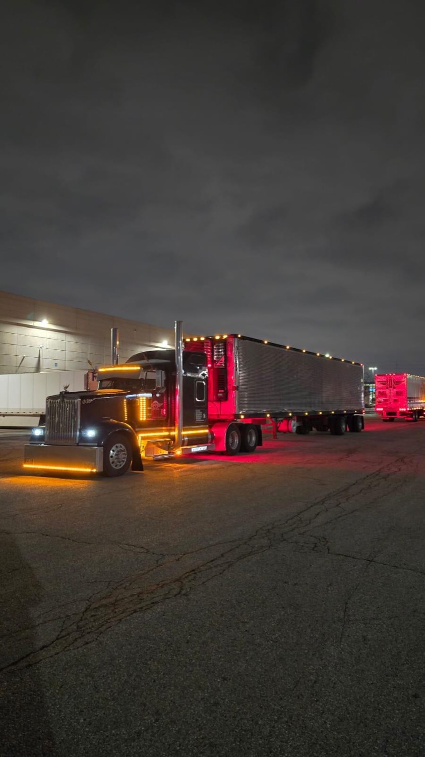 Black Kenworth W900 “007” with red and amber lights at a loading dock at night