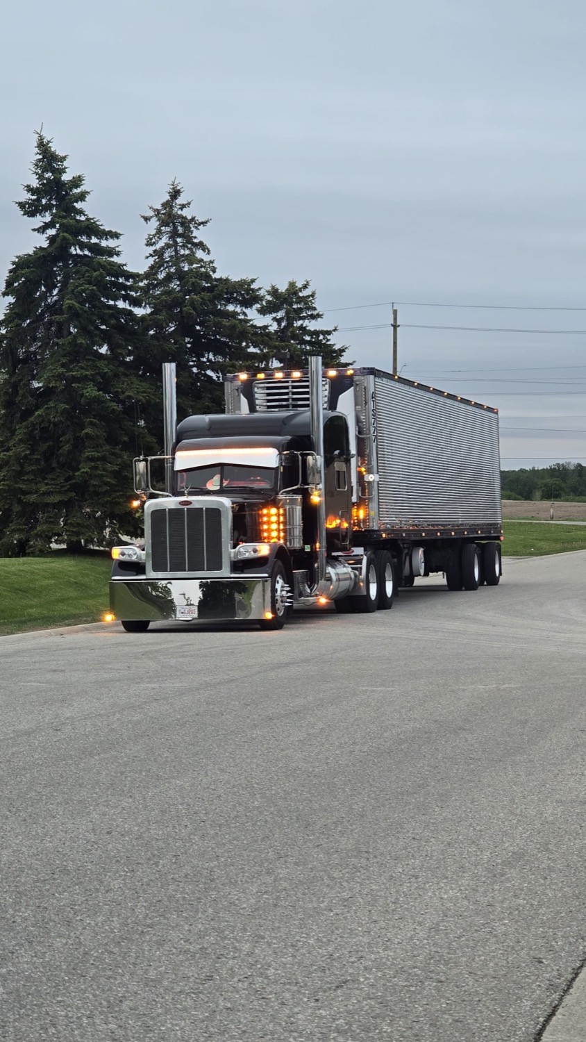 Black Peterbilt 389 with chrome stacks pulling a reefer trailer at dusk